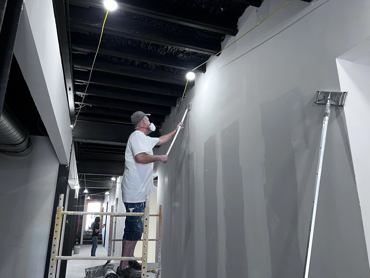 Commercial office corridor finish-out in progress, priming and cutting in near the exposed ceiling, Dallas, TX